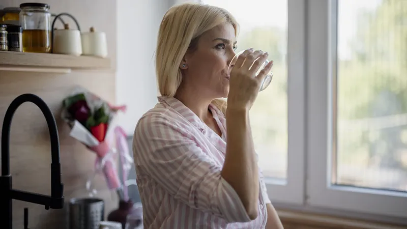 Woman drinking a glass of water by a kitchen window
