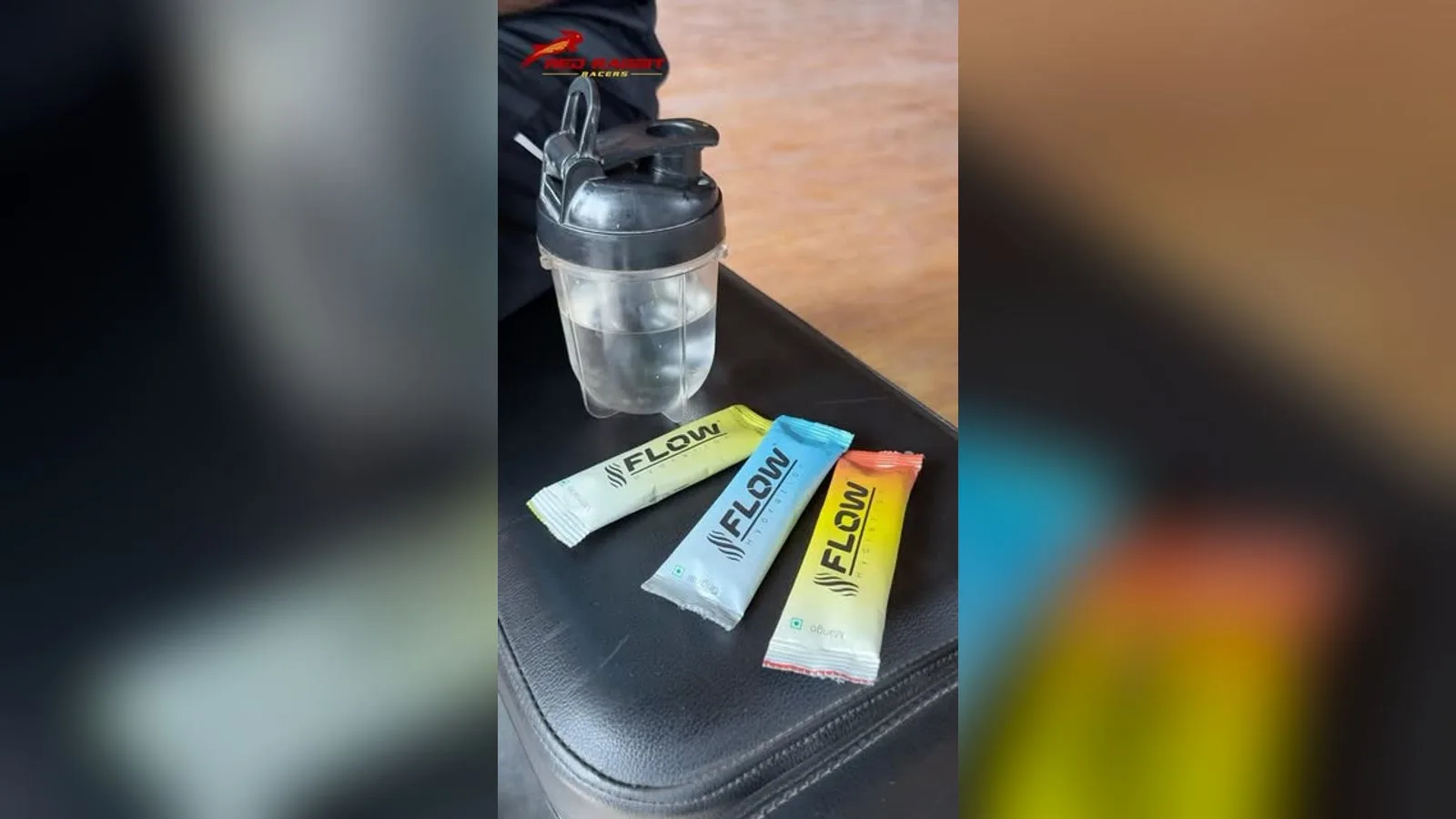 Three Flow electrolyte sachets on a black padded bench beside a shaker bottle of water