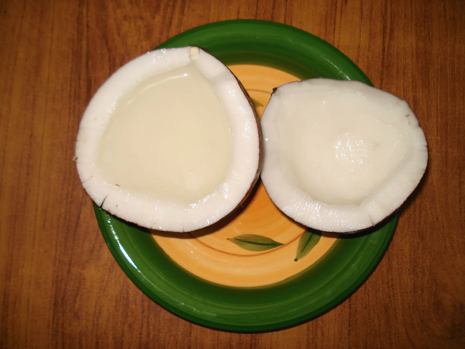 Two halves of a fresh tender coconut on a green plate, one holding coconut water and the other the soft white flesh