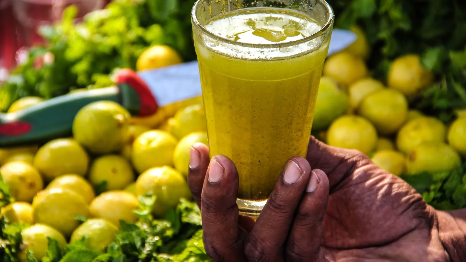 Hand holding a glass of nimbu pani over a heap of fresh lemons