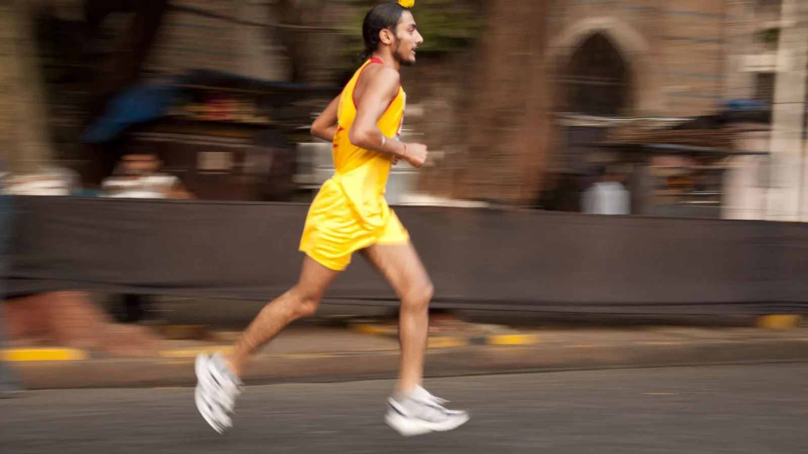 Runner in a yellow vest mid-stride at the Mumbai Marathon